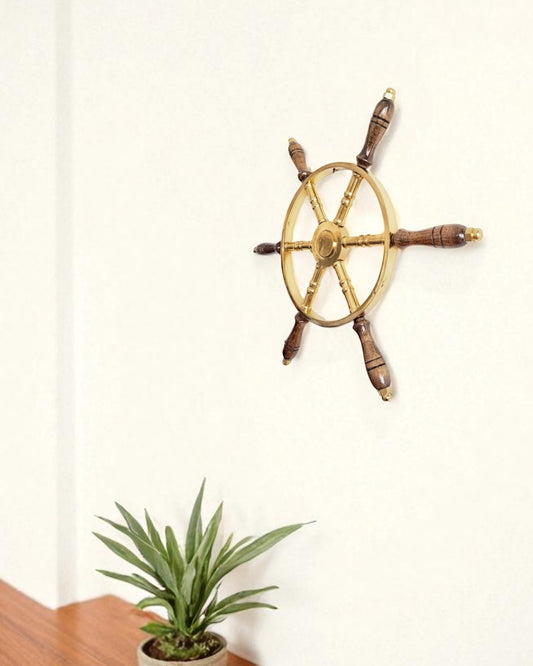 Decorative ship's steering wheel on a white wall with a potted plant in the foreground.