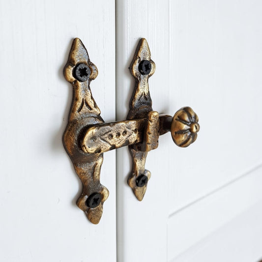 An ornate antique-style bronze door latch with a decorative knob, mounted on a white paneled door.