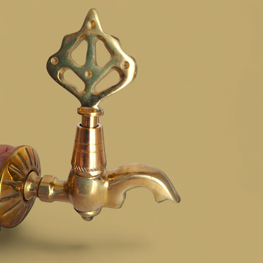 Brass faucet with decorative handle on a beige background