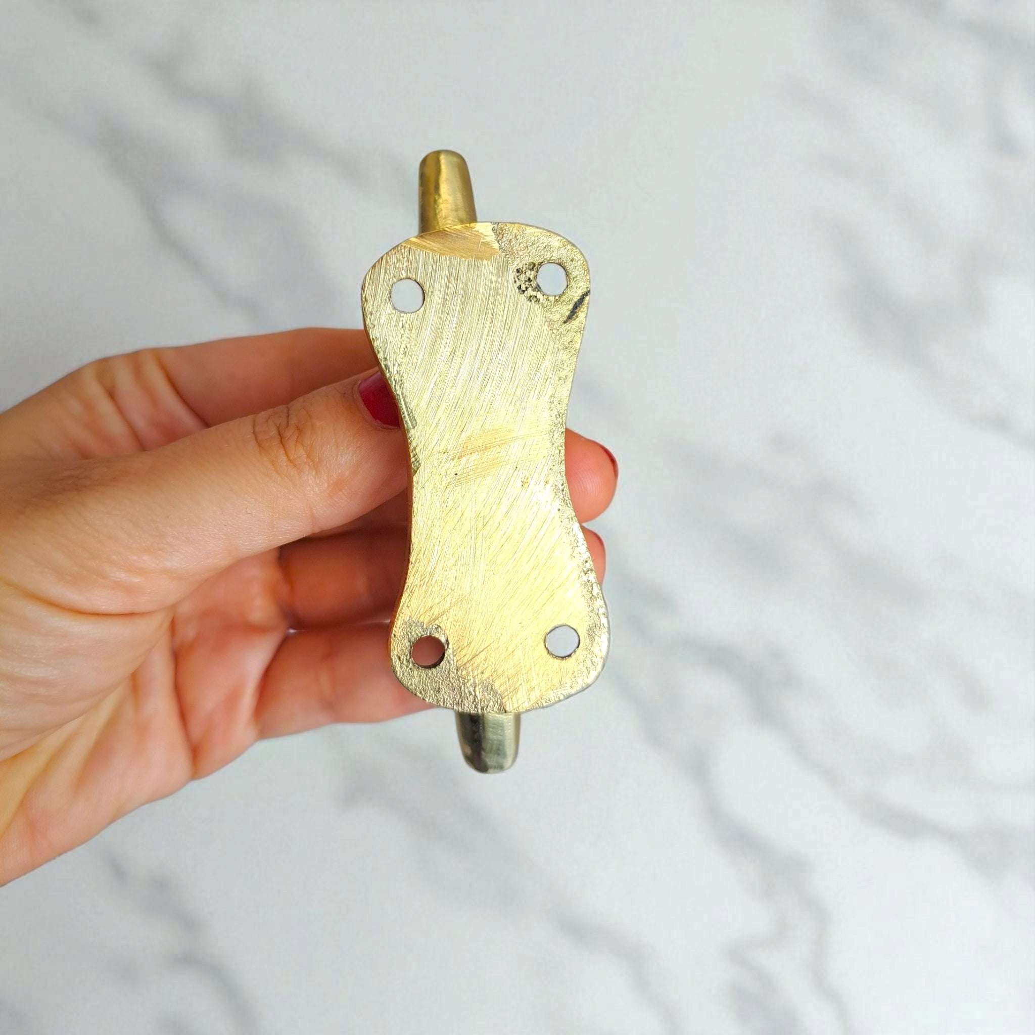 Hand holding a brass wall hook against a light gray background