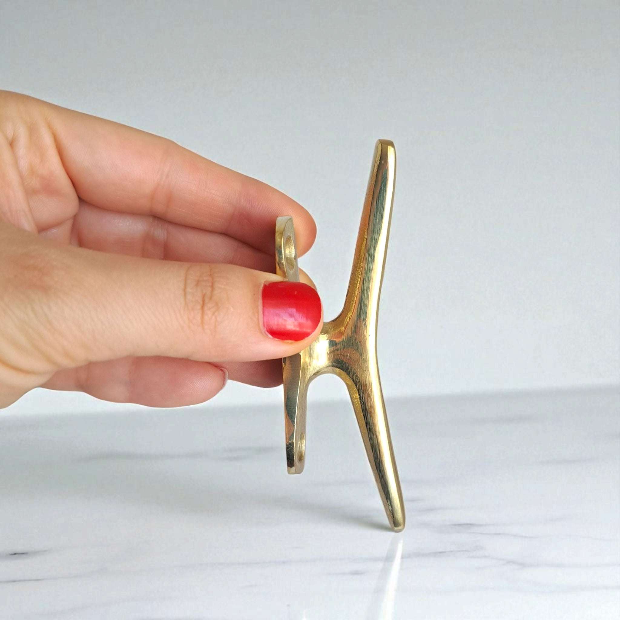 brass nautical cleat pinched by red fingernail, small decorative piece