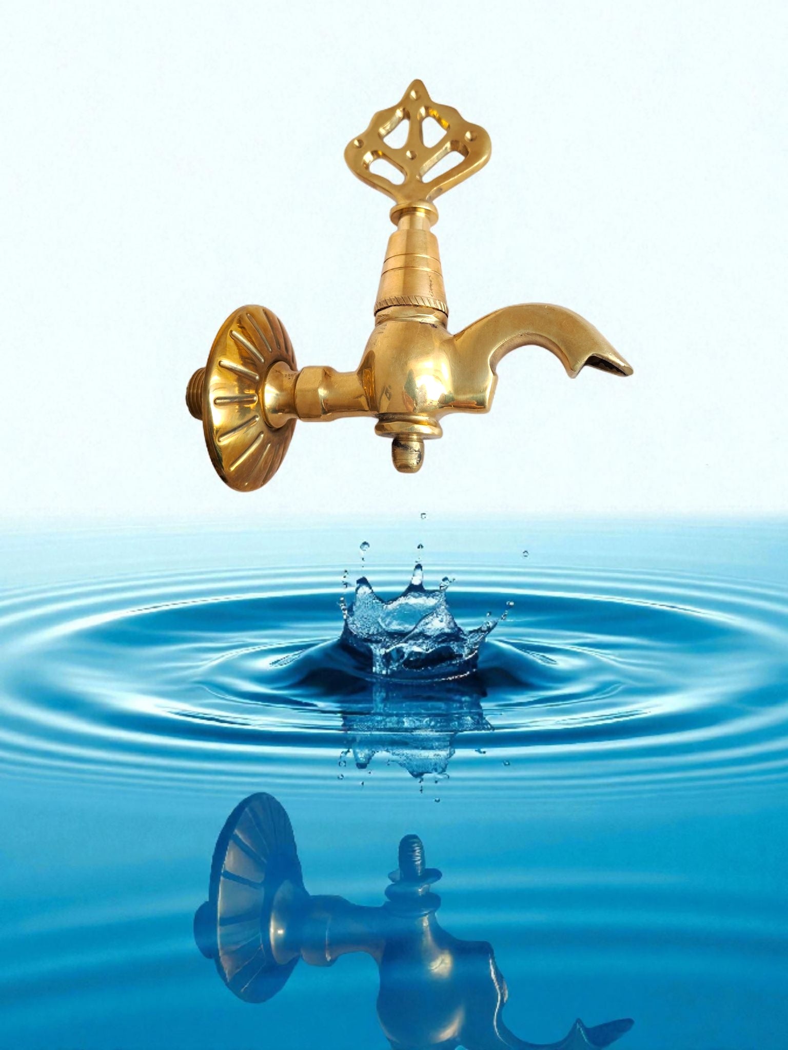 Gold faucet over water with a drop of water falling into the water, creating ripples.