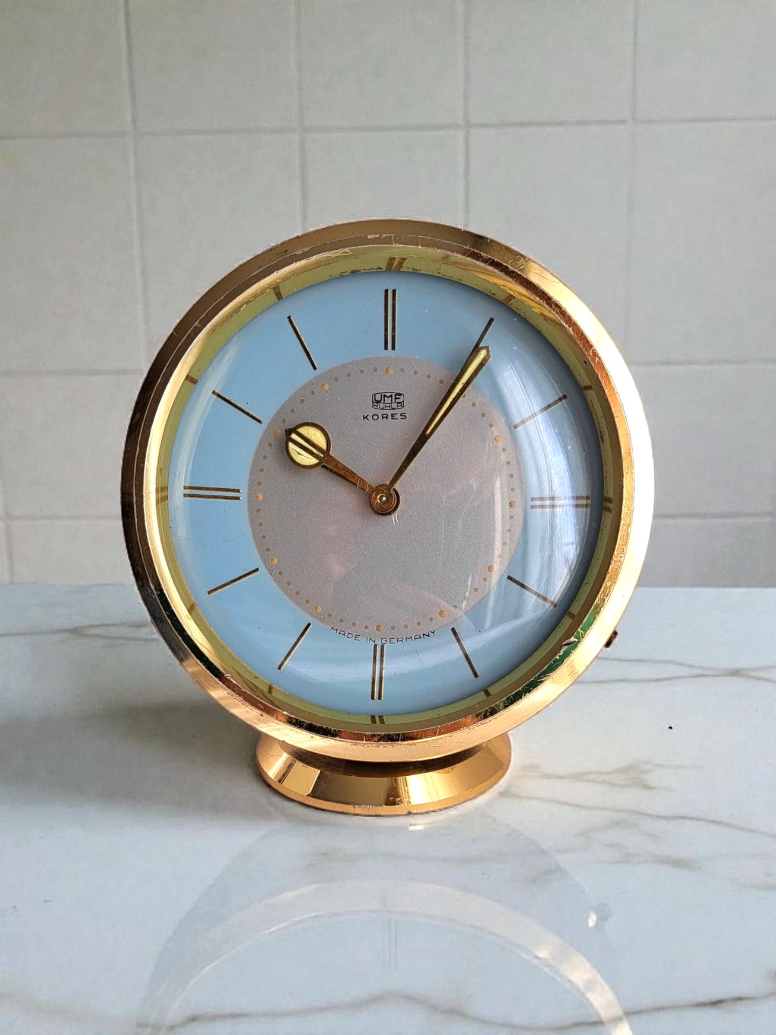 Gold-framed clock with a light blue face on a marble surface.