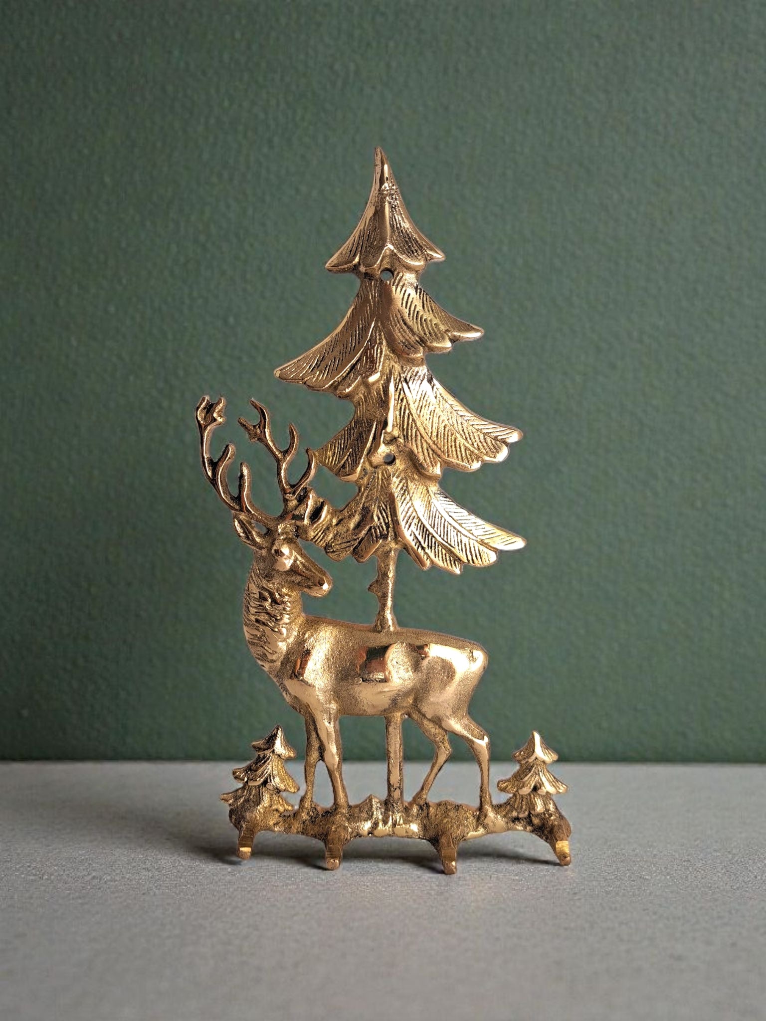 Brass deer and tree figurine on a gray surface with a green background
