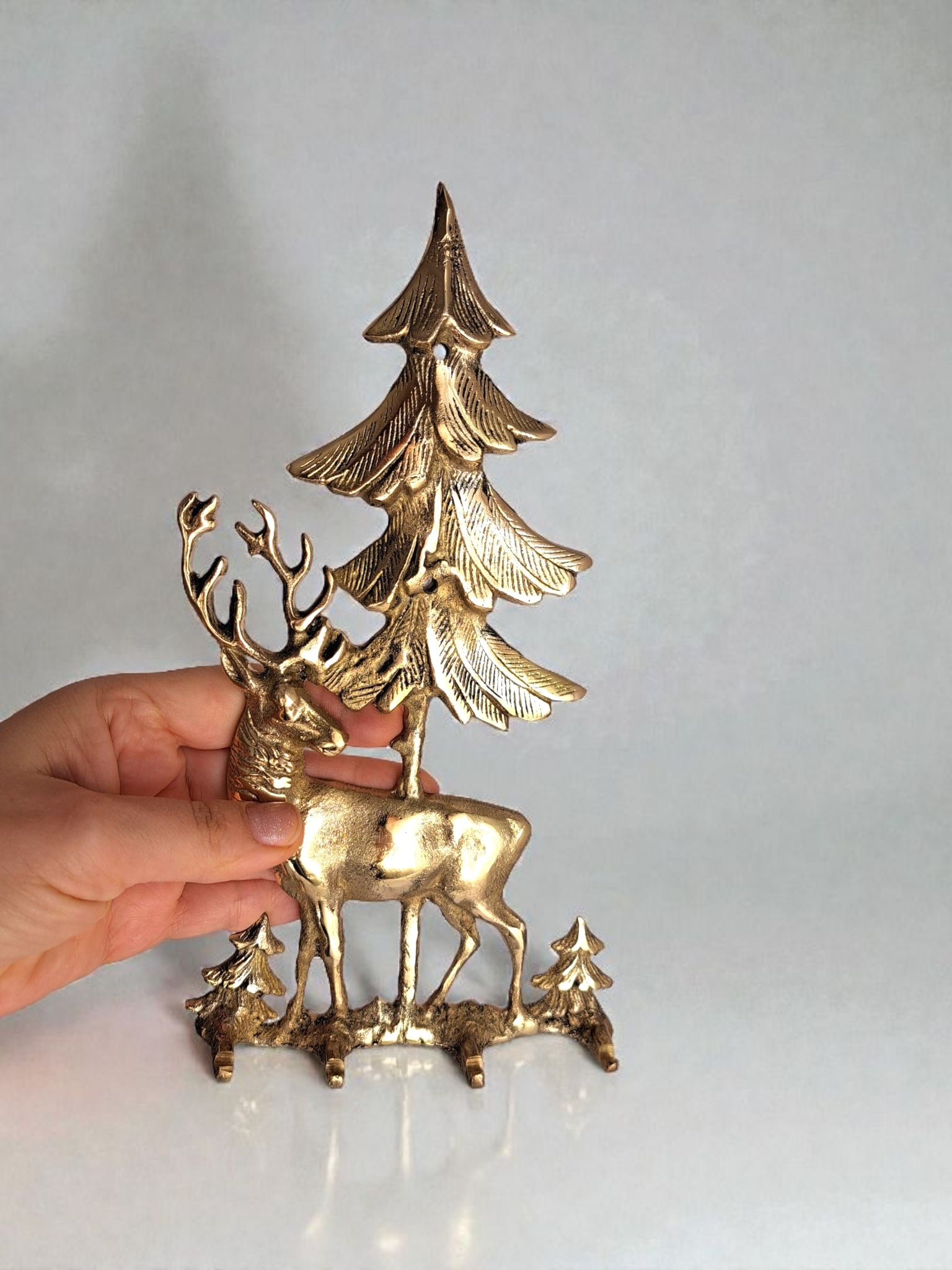 Gold deer and tree figurine held by a hand against a light gray background