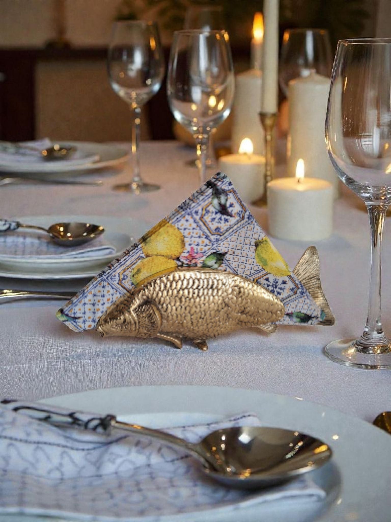 Decorative table setting with a fish-shaped napkin holder, lemon-themed napkin, and candlelight.