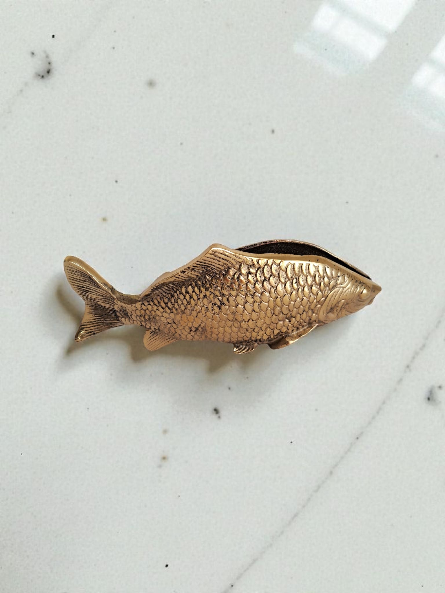 Bronze fish-shaped object on a marble surface