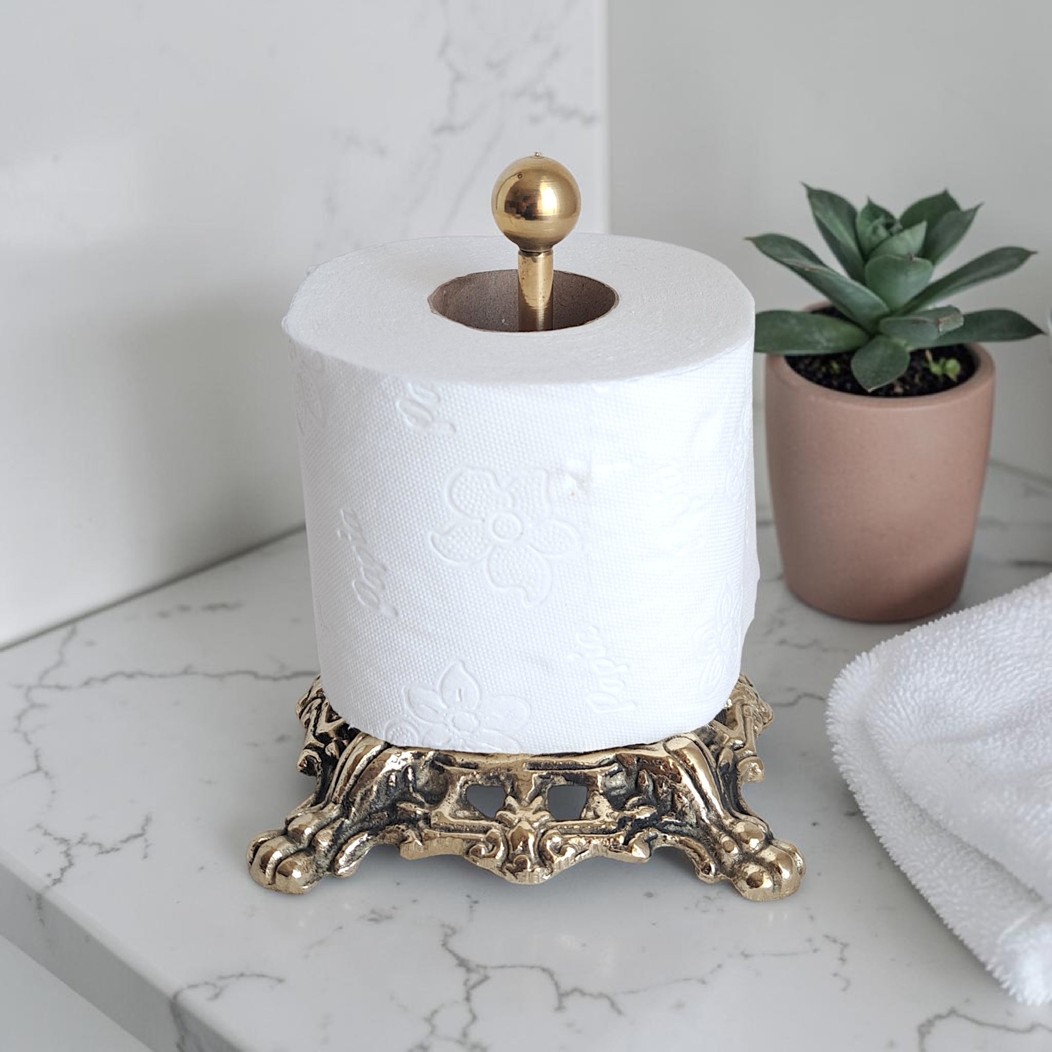 Decorative gold paper towel holder with a roll of paper towels on a marble surface.