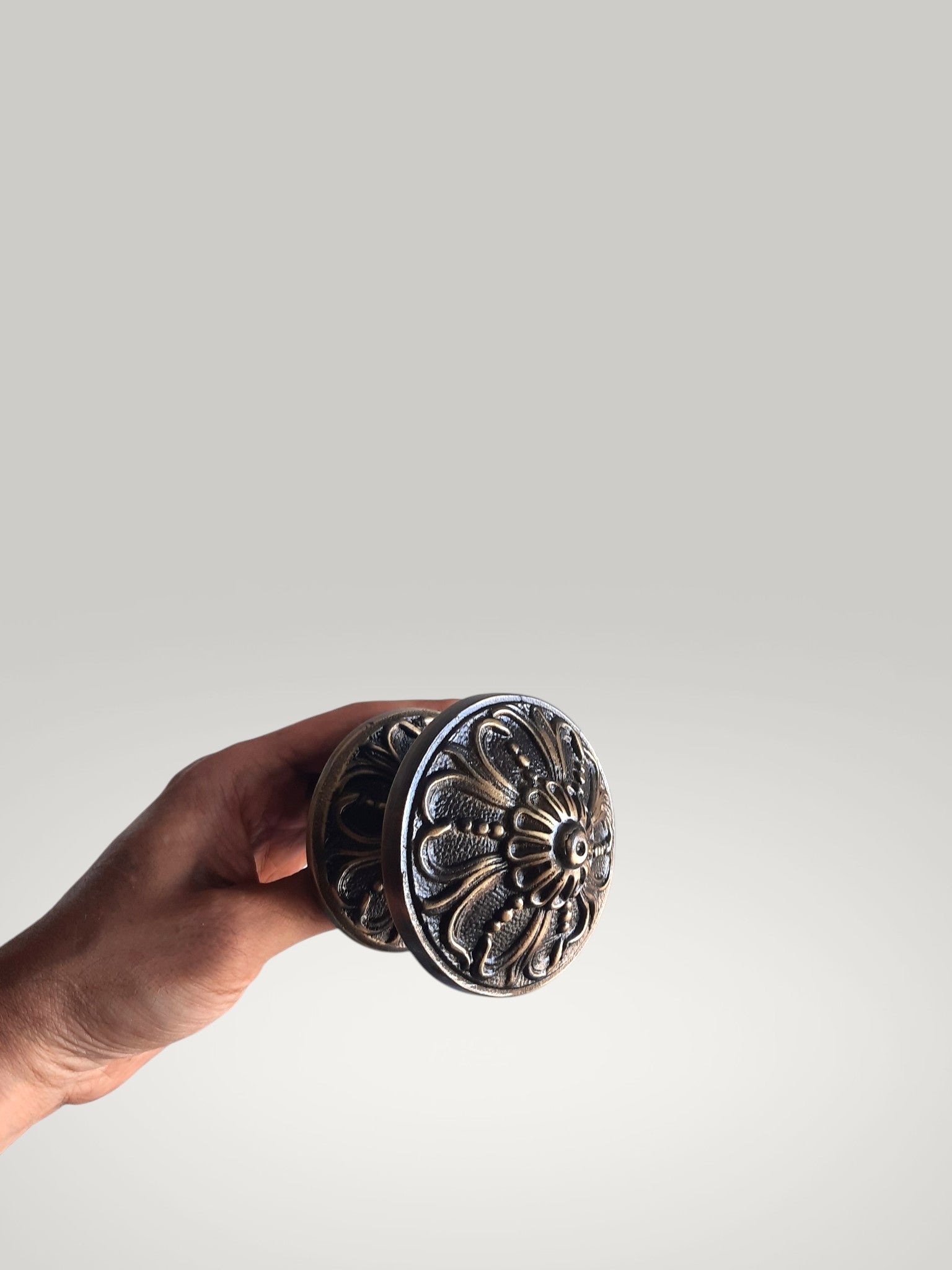 Hand holding a decorative metal knob against a plain background