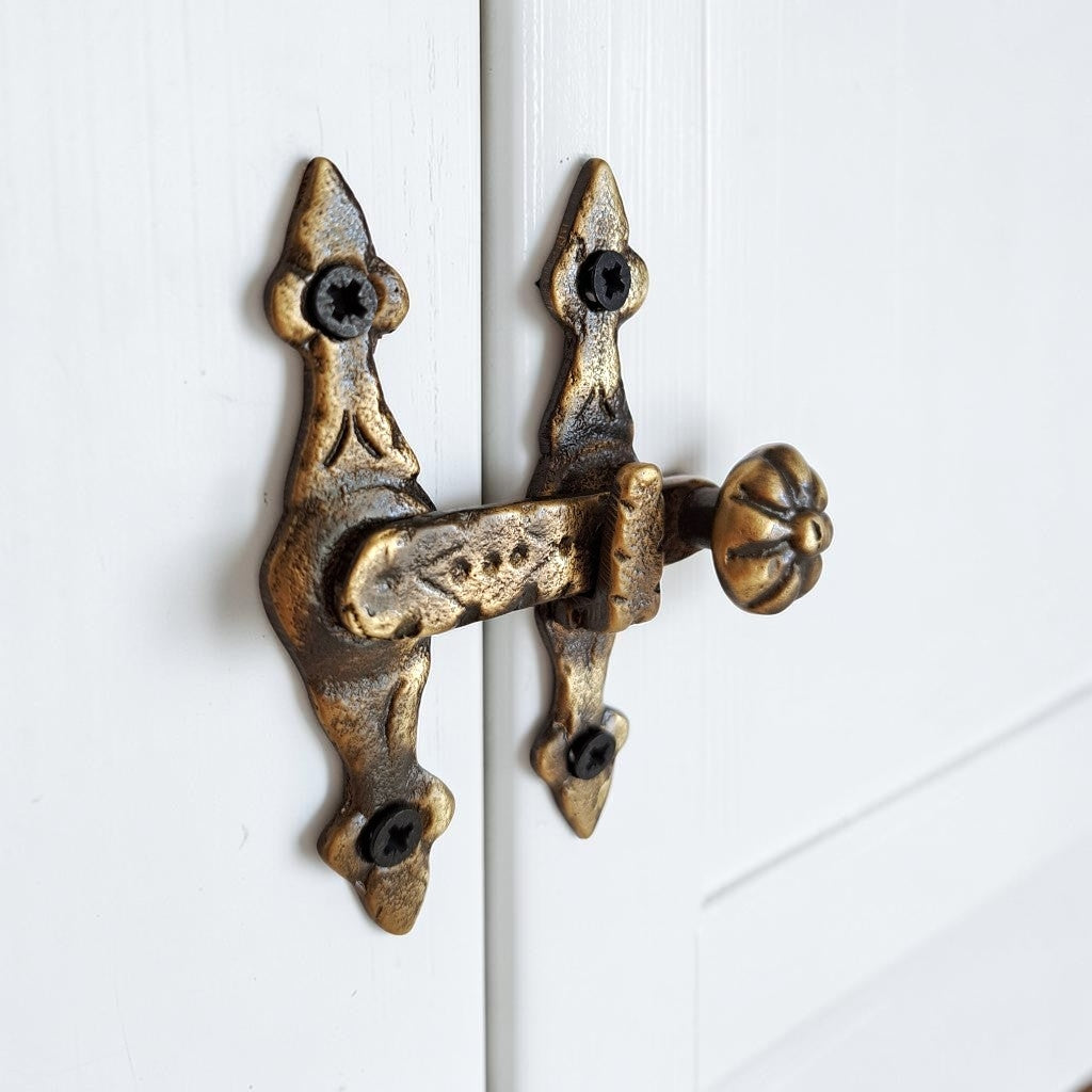 An ornate antique-style bronze door latch with a decorative knob, mounted on a white paneled door.