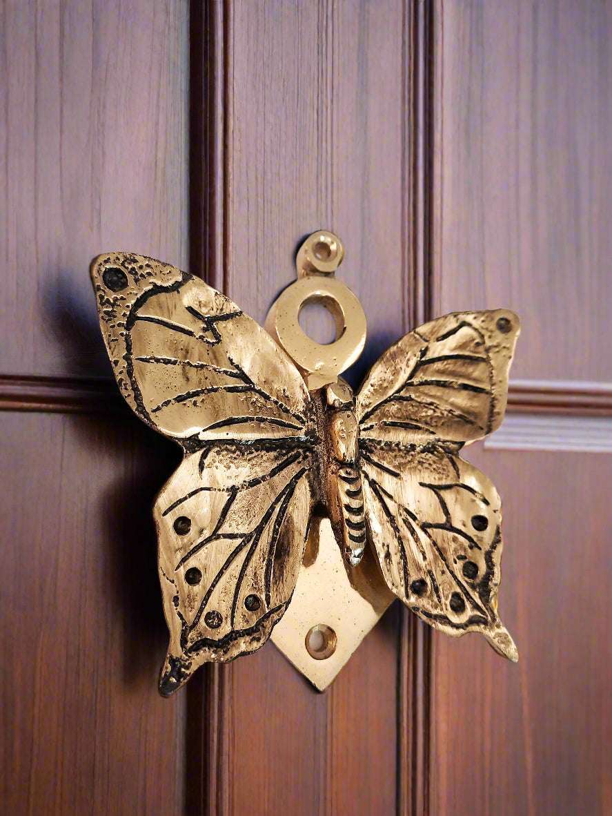 Butterfly shaped door knocker on brown wooden door, elegant door decor.