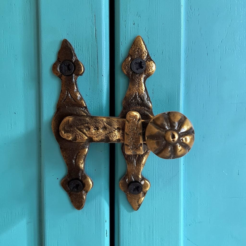 An ornate antique-style brass door latch with a round doorknob, mounted on turquoise painted wooden door panels.