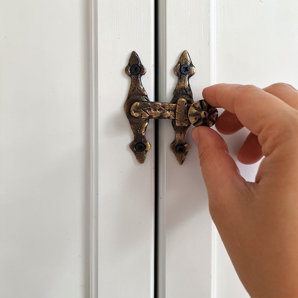A close-up of a hand adjusting an ornate antique bronze cabinet latch on white paneled doors.