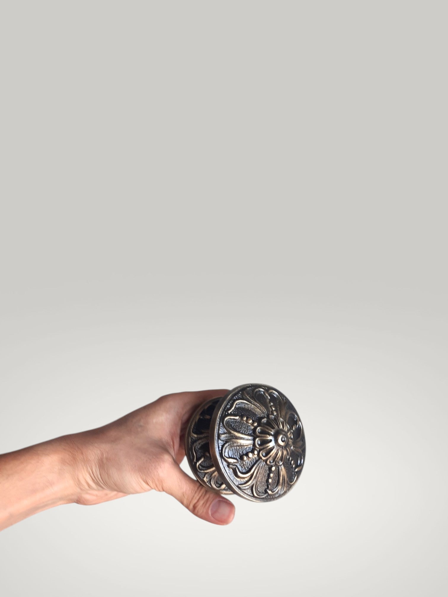 Hand holding a decorative metal knob against a plain background
