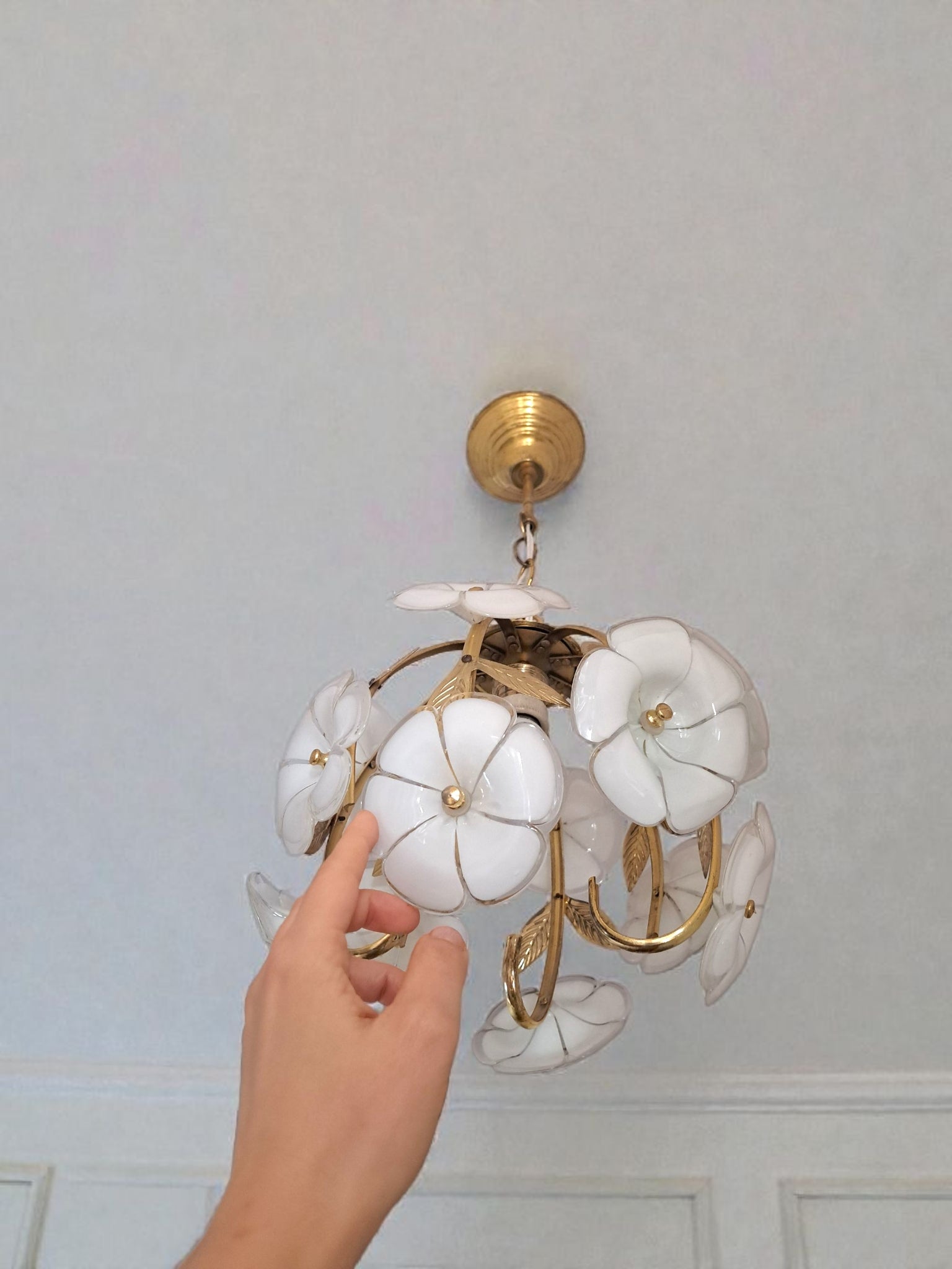 Decorative ceiling light fixture with white floral designs and gold accents, held by a hand against a light gray wall.