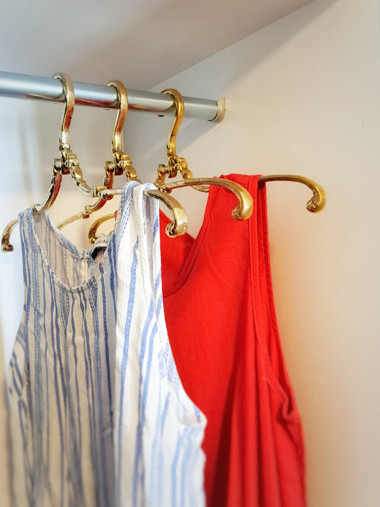 Gold hooks holding two shirts, one striped and one red, against a neutral background.