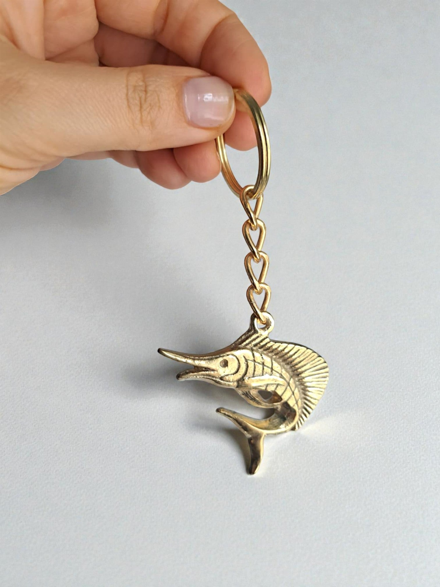 Gold fish-shaped keychain held by a hand on a light gray background