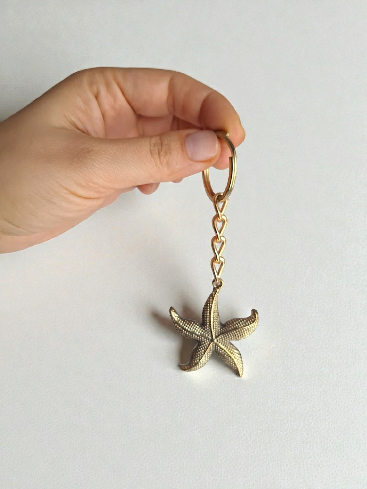 Hand holding a gold starfish keychain against a white background