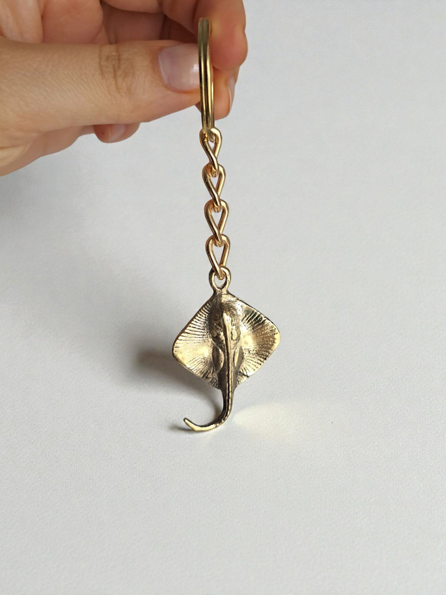 Gold stingray keychain held by a hand on a light gray background