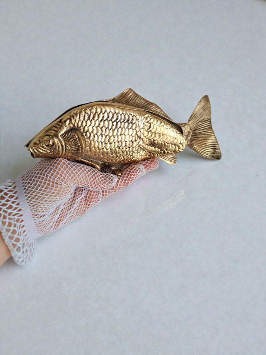 Gold fish-shaped object held by a gloved hand on a light background