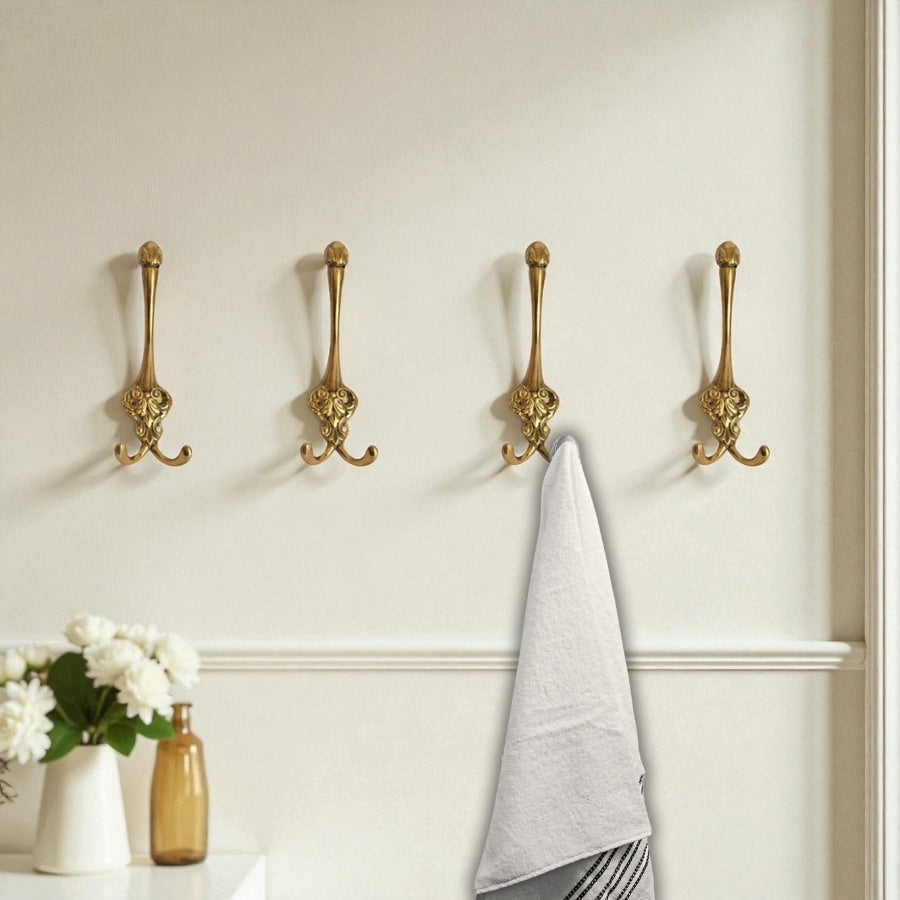 Four gold wall hooks on a white wall with a gray towel hanging from one of them.