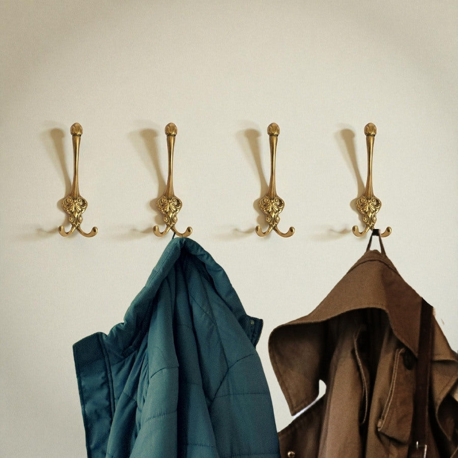 Four gold hooks on a beige wall with two coats hanging from them.