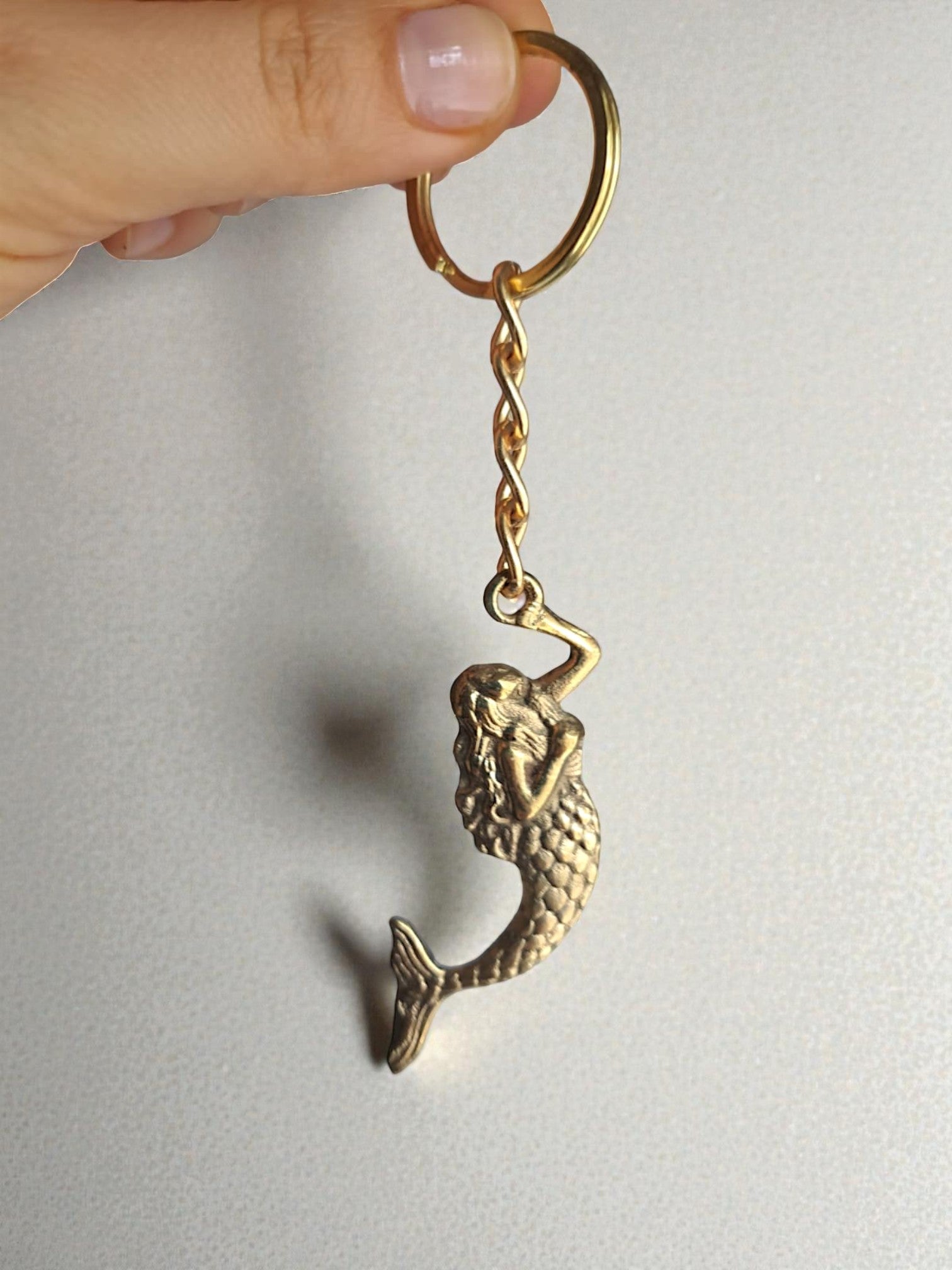 Gold mermaid keychain held by a hand on a light gray background