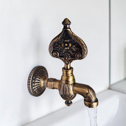 An ornate vintage-style wall-mounted faucet with a decorative handle and spout, shown with water flowing from the spout against a white tiled wall.