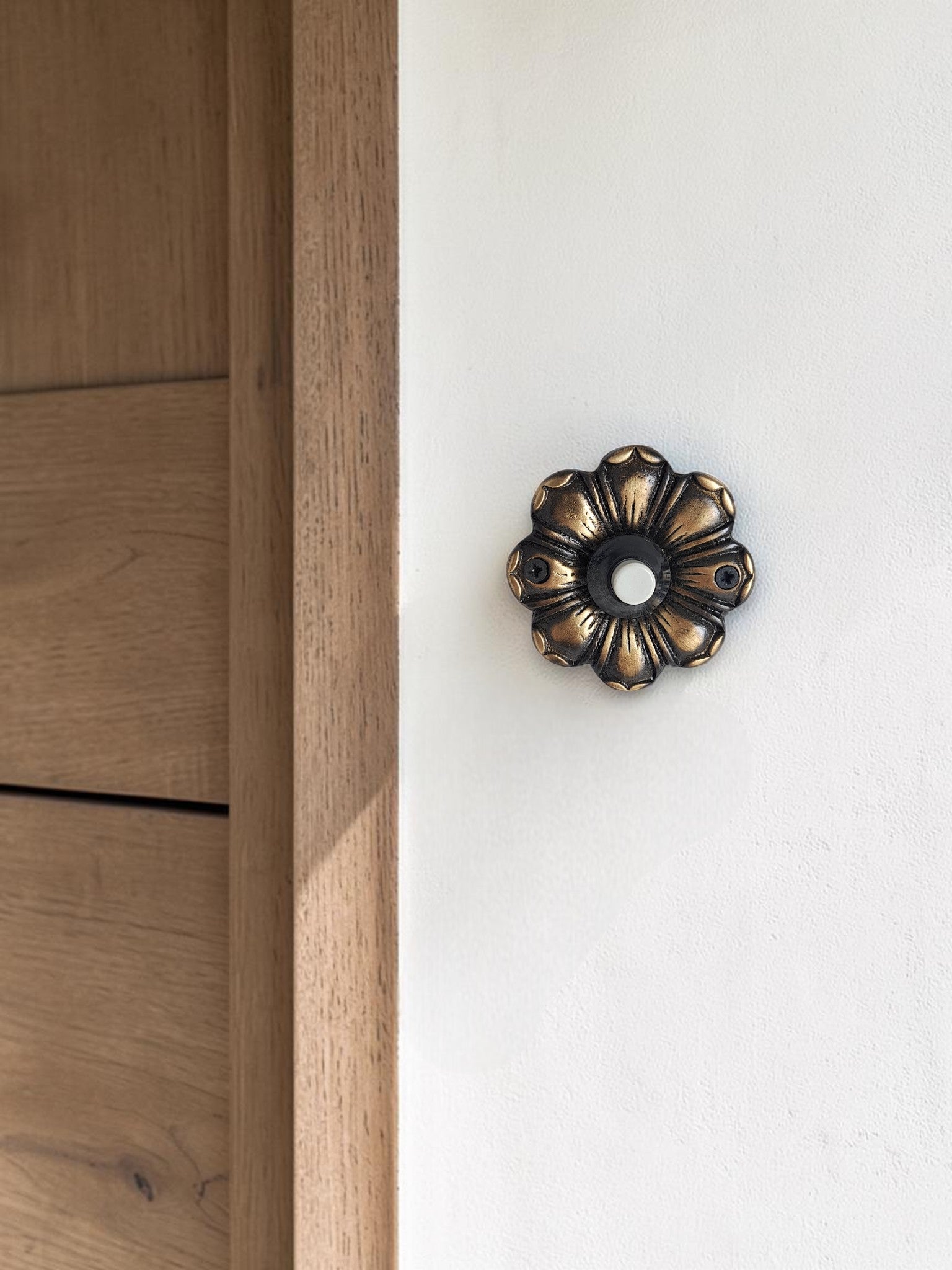 Antique gold brass doorbell mounted beside wooden front door