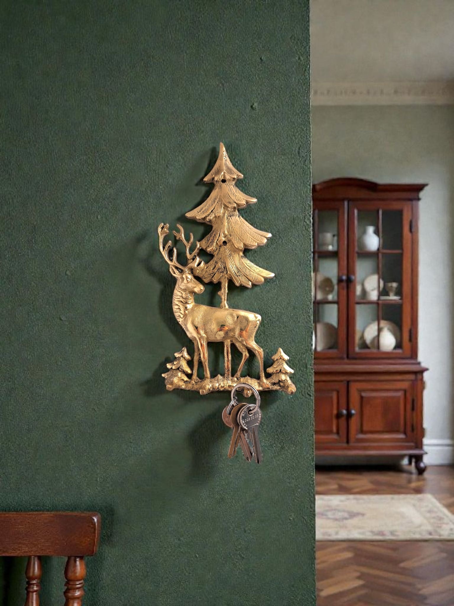 Decorative wall piece with reindeer and tree on a green wall, with a wooden cabinet in the background.